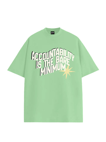 A light green short-sleeve t-shirt with a graphic text print reading 'ACCOUNTABILITY IS THE BARE MINIMUM' in white and black, accented by a yellow starburst on the front, shown against a plain white background 2026 protest cockroach janta party cjp
