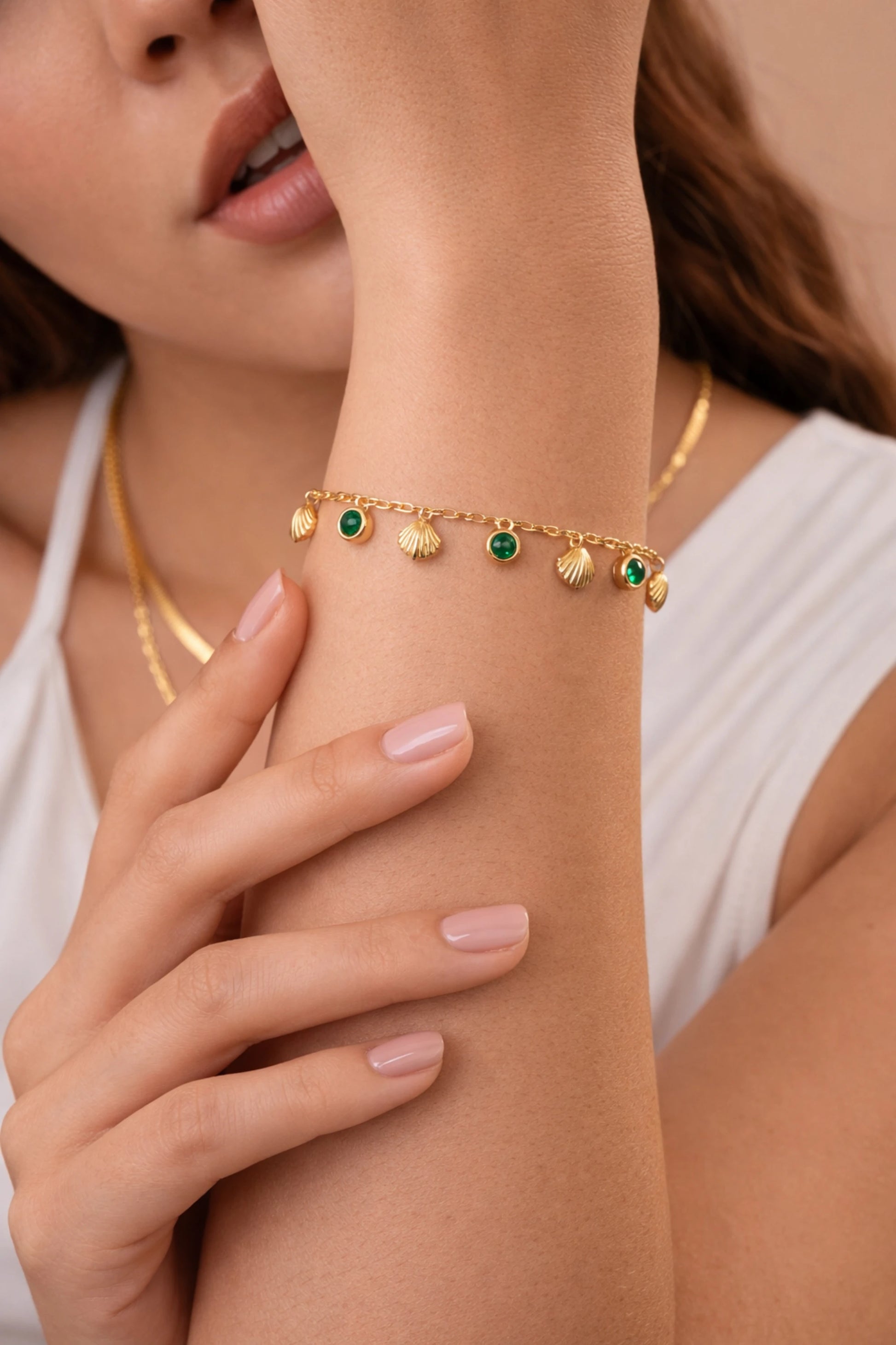 Close-up of a woman's arm wearing a  shell emerald gold bracelet