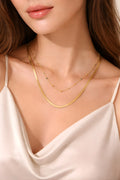 Close-up of a woman wearing a gold necklace with a white top.